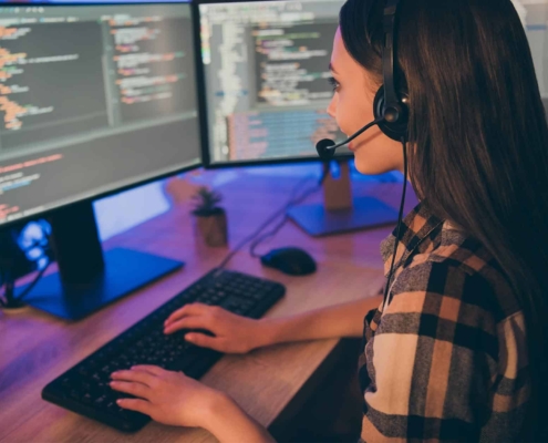 Person-analyzing-code-on-a-computer-while-talking-on-a-headset.