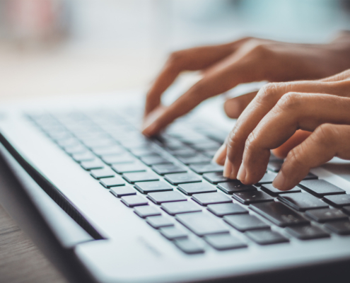 Side view of two hands typing on a laptop