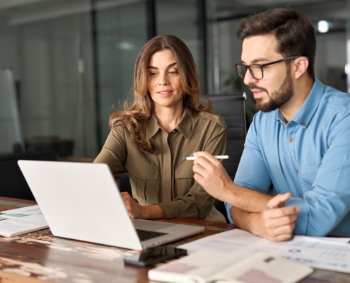 Two office workers at desk looking at laptop