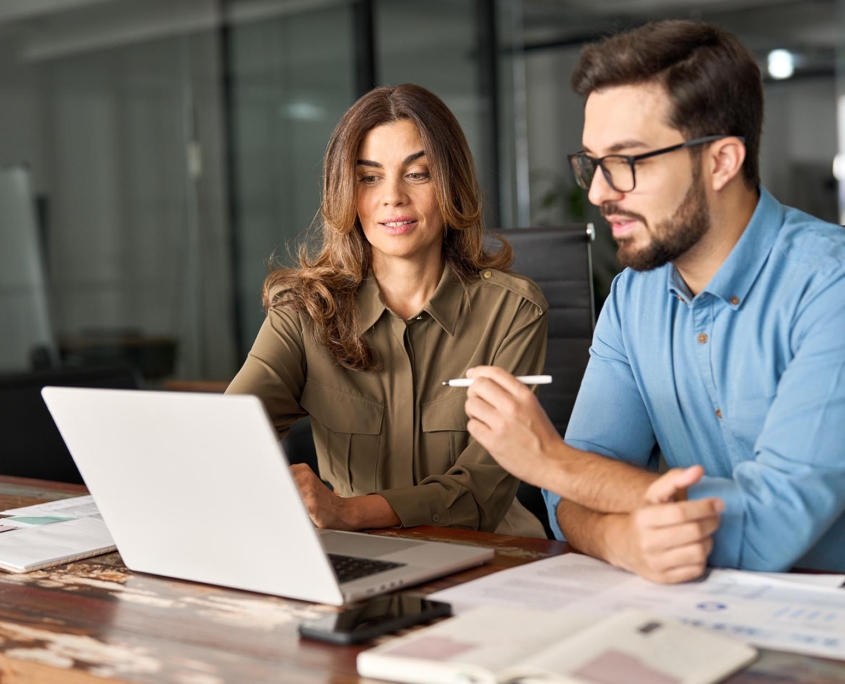 Two office workers at desk looking at laptop